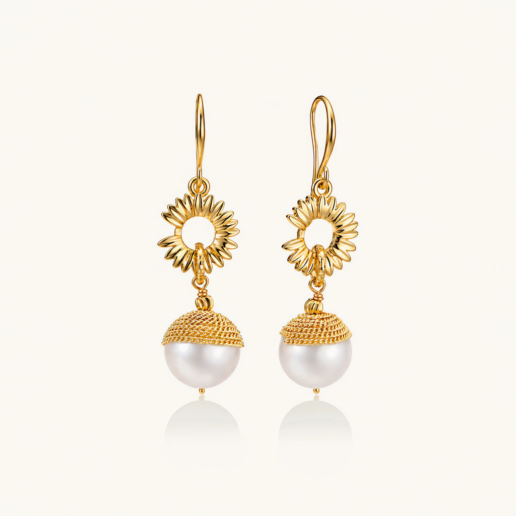 Gold sunburst charm earrings with baroque pearl drops on French hooks against cream background