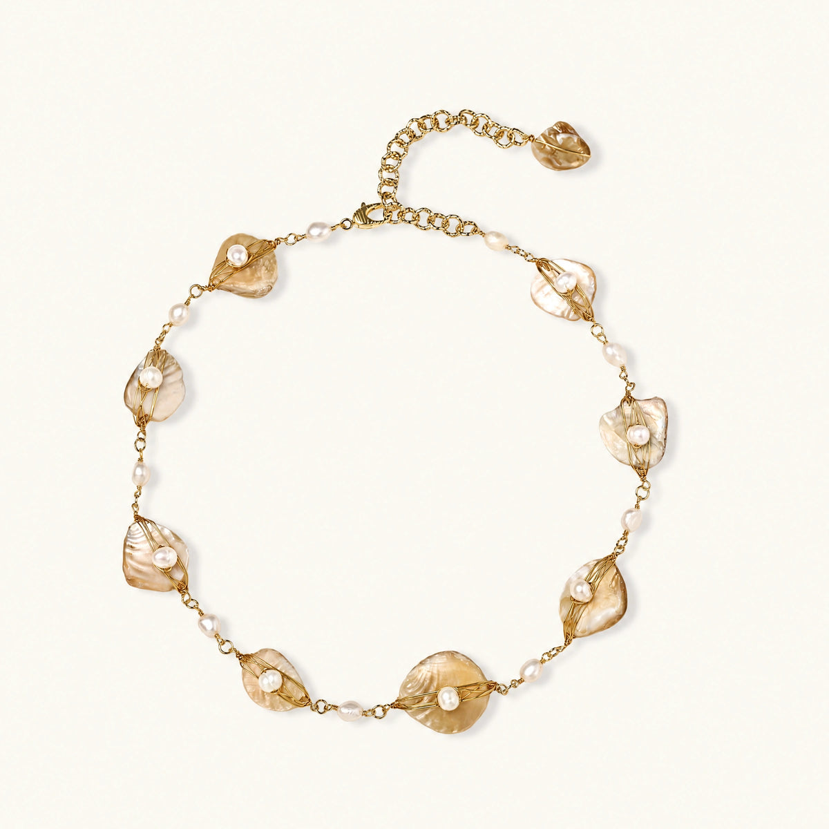 Gold-plated necklace with wire-wrapped shell pieces and freshwater pearls on neutral background, adjustable chain visible.