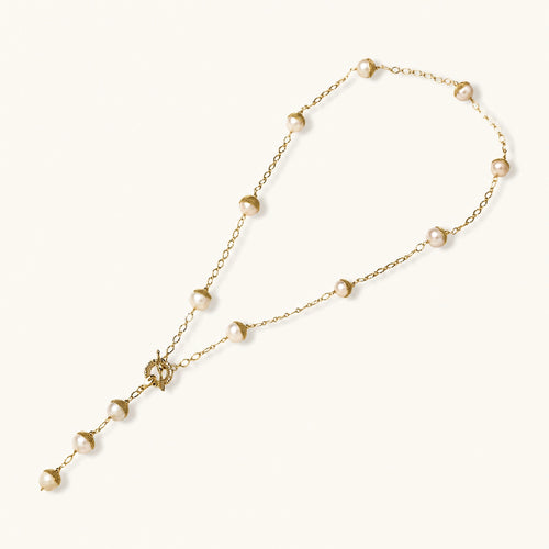 Gold-plated lariat necklace with baroque pearls and textured caps on cream background, showing adjustable Y-shaped design.