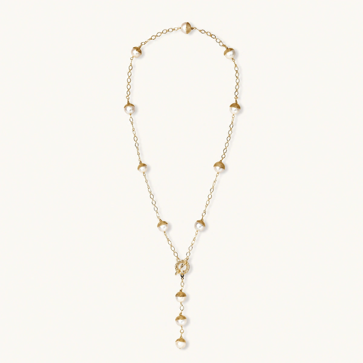Gold-plated lariat necklace with baroque pearls and textured caps on cream background, showing adjustable Y-shaped design.