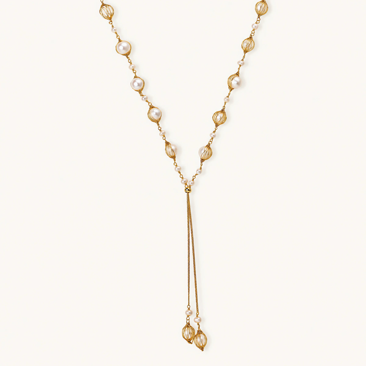 Adjustable gold lariat necklace with freshwater pearls nested in delicate cage settings and Y-shaped tassel drop